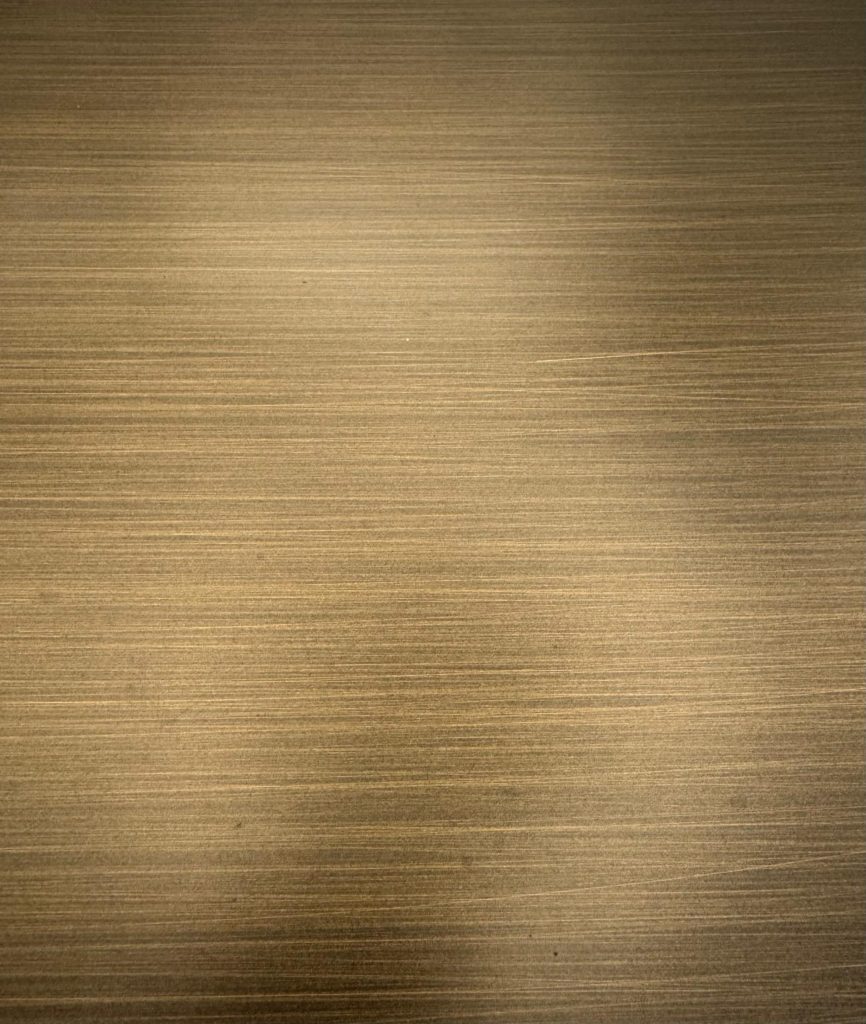 Superficie in alluminio trattata con finitura tinta ottone satinata, caratterizzata da tonalità calde e una texture morbida e uniforme. Una lavorazione raffinata che unisce leggerezza del materiale ed eleganza estetica, ideale per arredi su misura e dettagli architettonici contemporanei.